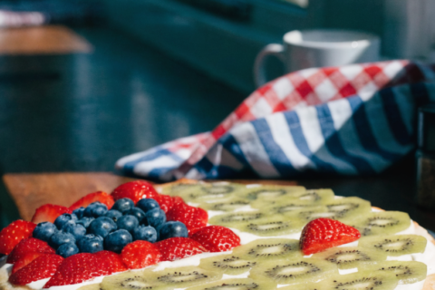Flag fruit pizza on a round pan with blueberries and strawberries arranged like a flag