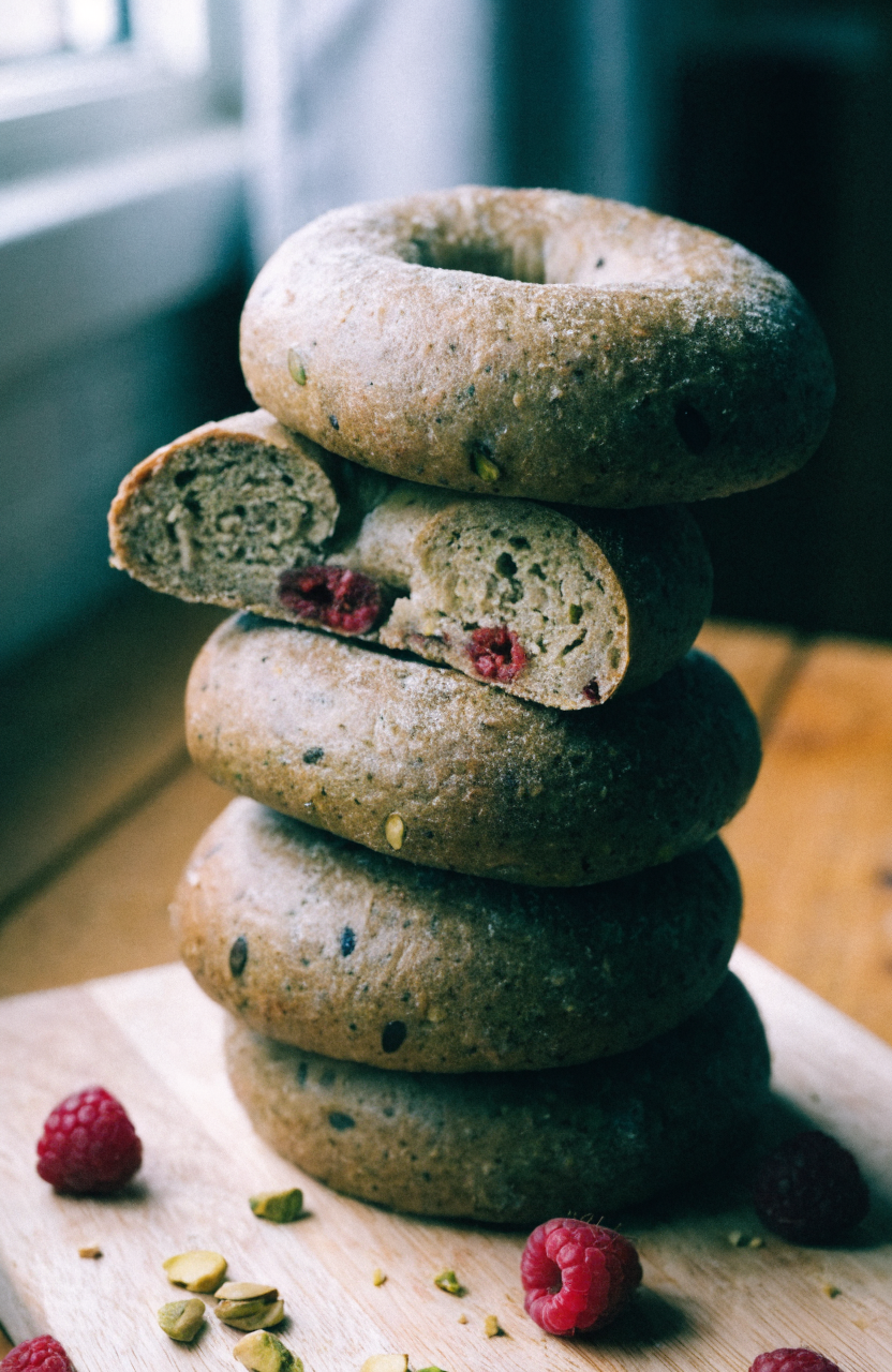 A stack of sliced raspberry pistachio sourdough bagels on a wooden board with visible raspberry ribbons and chopped pistachios